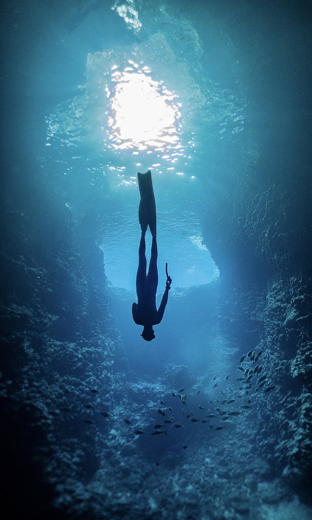 A silhouette of a freediver gliding through a vibrant underwater cave in Tonga.